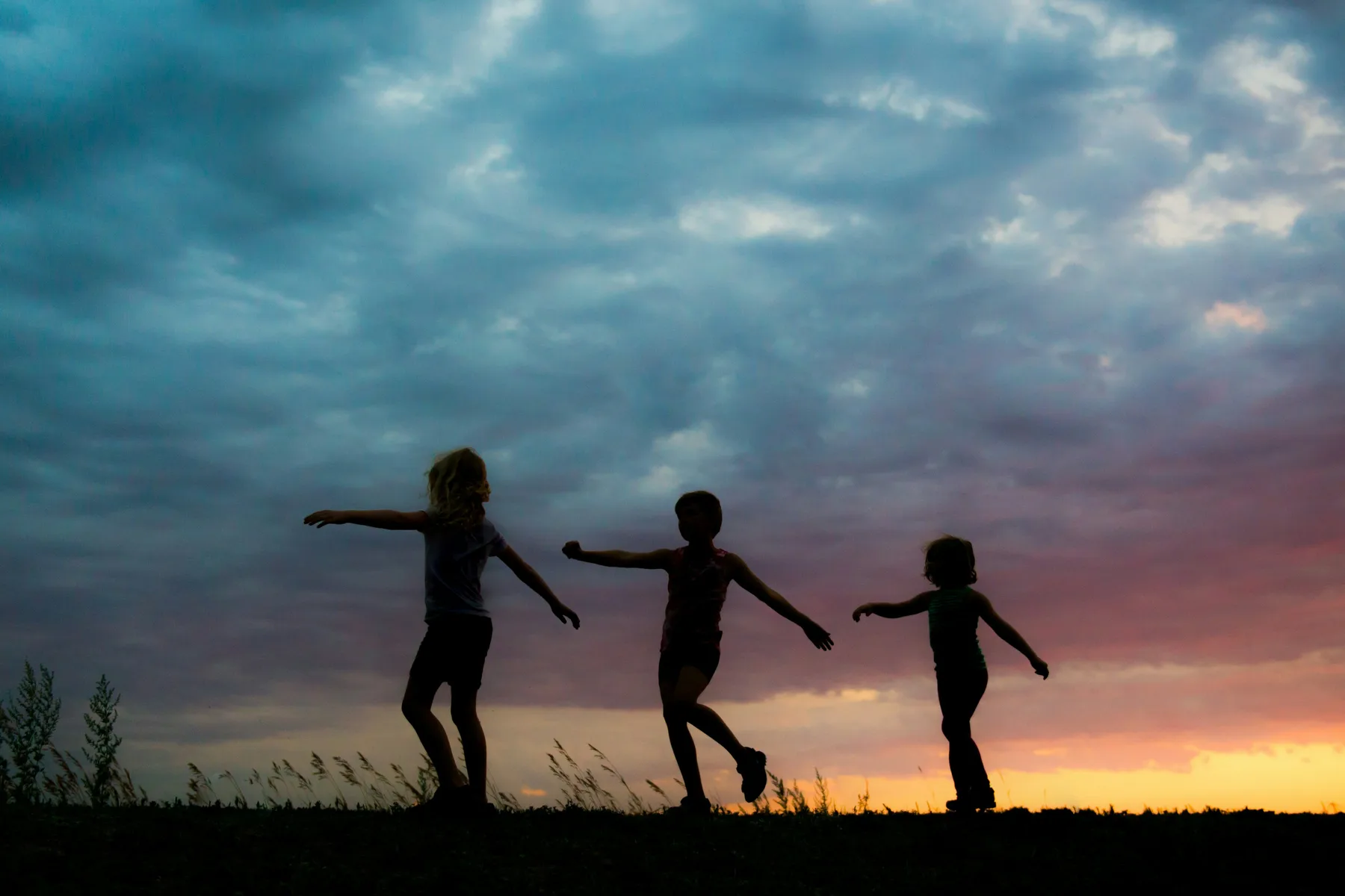 Trois enfants dansent en silhouette au coucher du soleil